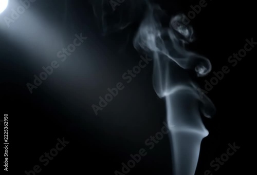 Graceful white smoke swirls against a dark background, illuminated by a soft light.
