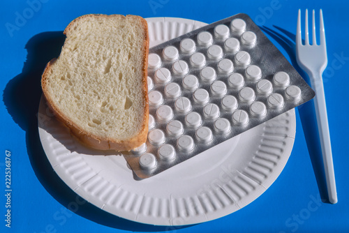 Bread on a paper plate with pills and a plastic fork on a blue background.