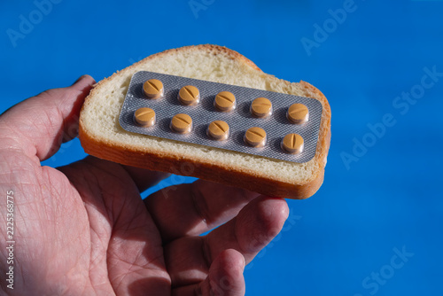 Hand holding bread topped with a blister pack of pills on a blue background.