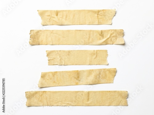 Torn strips of beige adhesive tape arranged vertically on a clean white background during a studio shoot