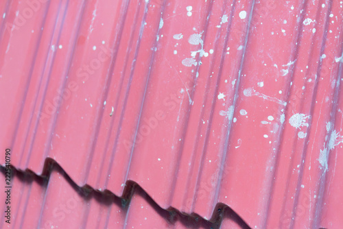 Closeup of red corrugated metal roof sheet with white paint splatter and diagonal ridges, weathered texture background