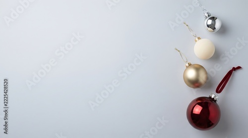 A refined holiday composition featuring ruby-red, champagne-gold, ivory, and silver Christmas baubles suspended in a vertical arrangement along the right side of a pale gray background.