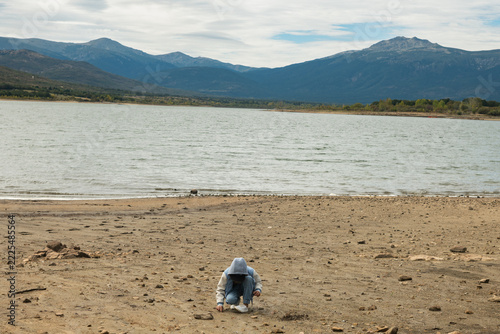 Child crouching on dry reservoir shore with low water level