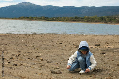 Child crouching on dry reservoir shore with low water level