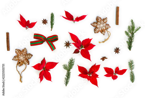 Christmas flat lay with red poinsettia, gingerbread cookie, spices, and fir branches, red and green bow on white background