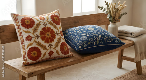 Embroidered floral decorative cushions on a rustic wooden bench in a cozy bright living room.