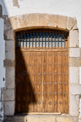 A traditional wooden door with decorative metal studs, framed by stone masonry and topped with a barred transom window.