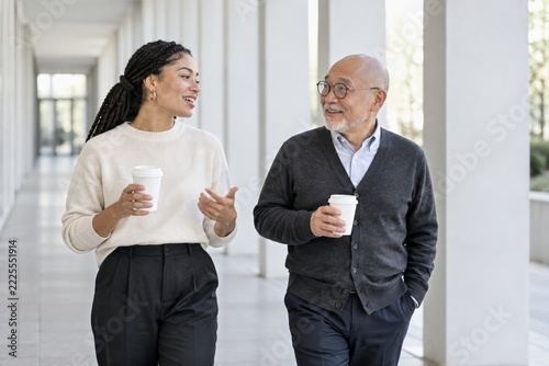 Coworkers chatting with takeaway coffee while walking through a bright corridor