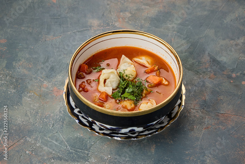 A bowl of spicy tom yum soup garnished with herbs and shrimp