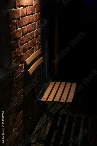 A sad lonely empty chair against a brick wall under lamp light with deep shadows at night time