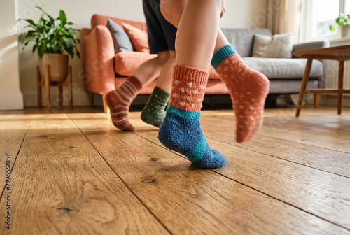 Children in colorful socks running across a wooden living room floor, low-angle motion view