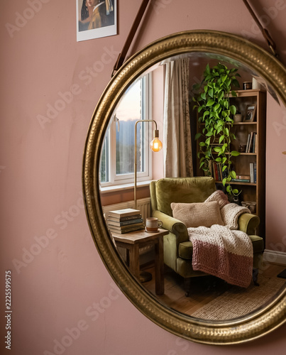 Cozy bedroom reading corner with armchair and plants reflected in a round mirror