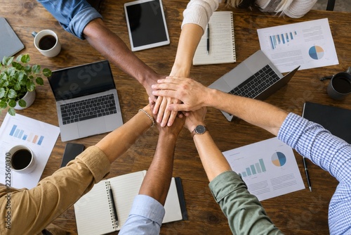 Overhead team stacking hands among laptops reports and coffee cups