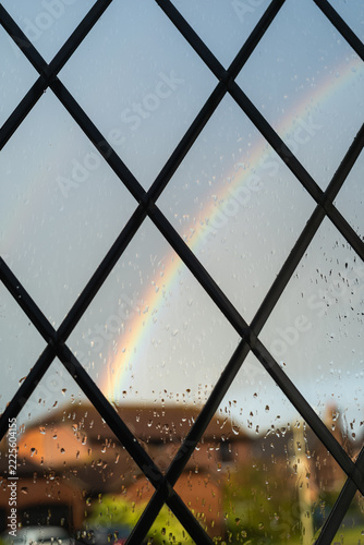 Leaded lights diamond style window on a wet day, with defocused rain and a rainbow over a red brick house.