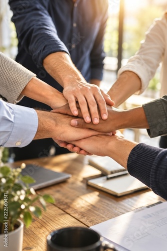 Close up of colleagues stacking hands in warm sunlight above an office table