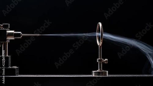 Smoke Ring Airflow Experiment Using Metal Apparatus to Create Visible Vortex Against Dark Background with Fluid Motion and Pale Smoke