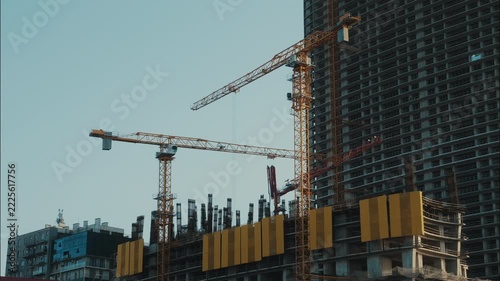 Tower cranes rotating at construction site in timelapse, heavy machinery operating beside unfinished high rise building and exposed concrete columns, structural engineering and urban development.