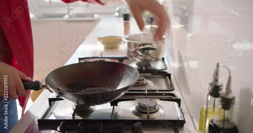 Home cook is tilting oil bottle, pouring into wok on front-burner to heat oil, partner arriving