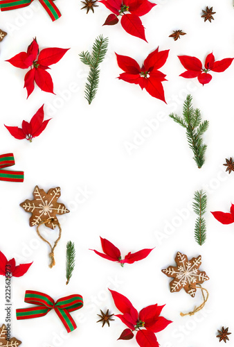 Christmas flat lay with red poinsettia, gingerbread cookie, spices, and fir branches, red and green bow on white background with space for text