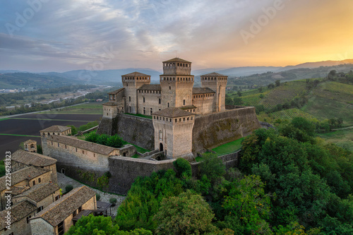 Aerial view of Torrechiara Castle and village on a hilltop at golden hour with sun flare over the Parma countryside