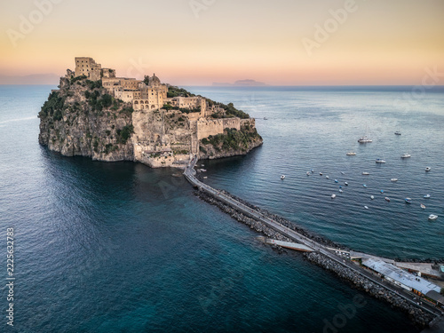 Ischia Aragonese castle at golden hour. ISCHIA, ITALY - OCTOBER 4, 2026: High angle view of the Aragonese Castle perched on a rocky islet with stone causeway and boats floating in the sea at golden ho