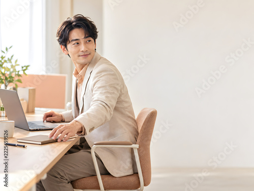 ビジネスシーンでノートに手を伸ばしながら振り返って微笑む男性 明るいオフィスの柔らかな自然光と右側に広がるコピースペース