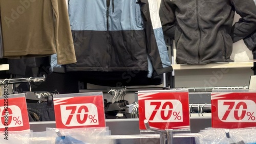 Obraz na plátně Close-up of red “70%” sale signs on a clothing rack; jackets and fleece tops are visible in the soft‑blurred background