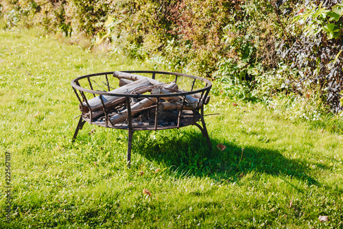 Round Metal Fire Pit Filled with Firewood in a Sunny Green Garden
