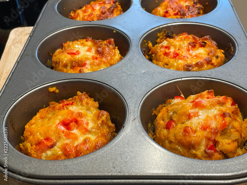 Golden savory muffins bake with melted cheese and red pepper in a metal muffin pan