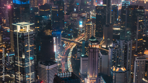 Aerial view of the illuminated Jakarta skyline at night with dense skyscrapers, glowing office buildings, and busy traffic trails on the roads below in Jakarta, Indonesia.