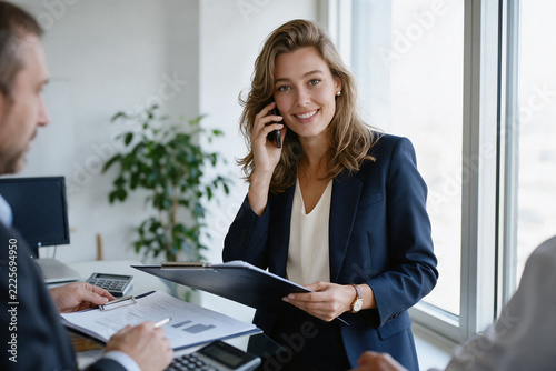 Businesswoman on phone call by office window holding clipboard