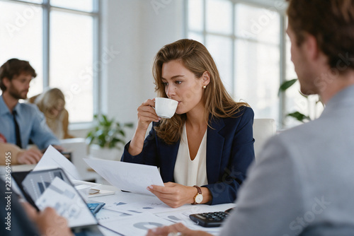 Woman sipping morning coffee and reading report at office desk