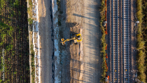 Aerial view of an excavator working on a new railway construction project with tracks and dirt paths in Milan, Lombardy, Italy.
