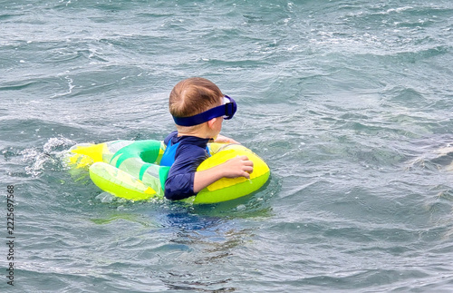 A preschool-aged boy learns to stay afloat using a yellow inflatable ring.