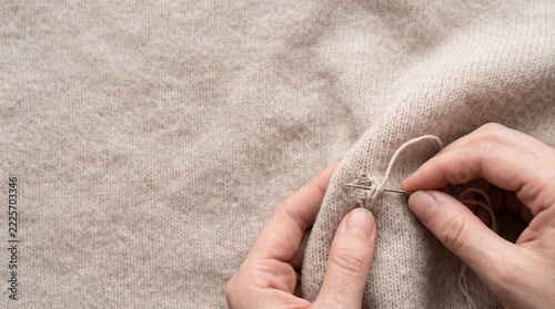close-up of hands mending a hole in a cashmere knit fabric, concept of sustainable fashion, clothing repair, and textile care