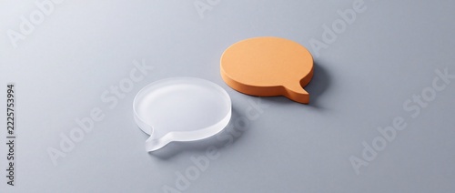 Two speech bubble icons, one clear and translucent, the other orange and textured, symbolizing communication, ideas, and conversation on a gray background