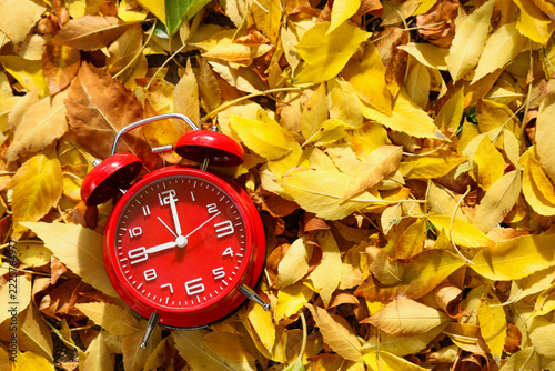Daylight saving time and seasonal change, red alarm clock on yellow autumn leaves time management and transition in the fall season