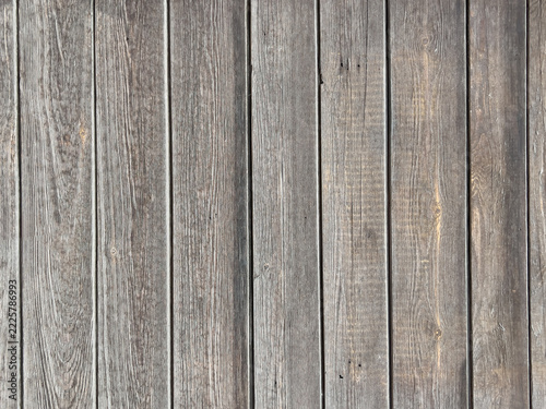 Weathered wooden plank panel with vertical grain texture and aged gray brown patina, close-up detail for background and surface use, rustic flooring or siding material sample