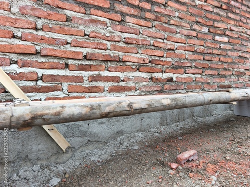 Unfinished red brick wall with horizontal wooden beam and concrete foundation on active construction site, ideal for civil engineering, masonry building, and house structure stock photo.