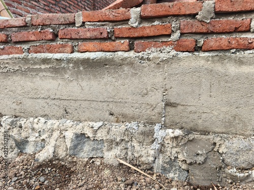Close up view of building foundation with stone masonry, concrete tie beam, and unfinished red brick wall on construction site, ideal for house structure material and civil engineering photo.