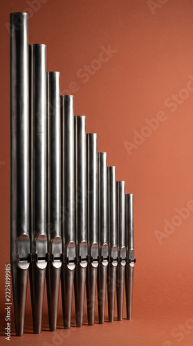 Vertical Array of Metal Pipe Organ Tubes Against Warm Orange Terracotta Wall