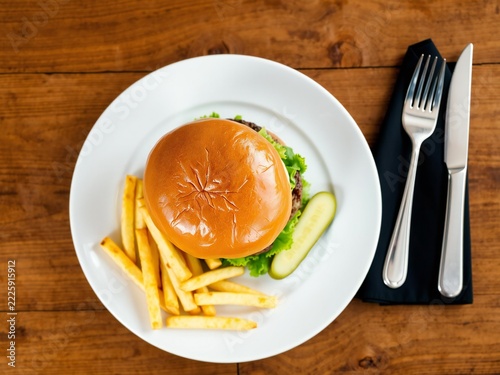 Delicious cheeseburger with crispy french fries on a white plate served on a rustic wooden table with cutlery