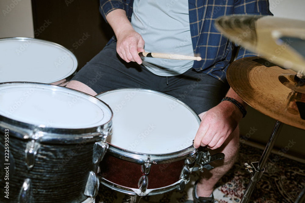 Fototapeta premium Young adult Caucasian male drummer playing acoustic drum set during rehearsal with wooden drumstick, close up. Image suitable for music festival promotion, audio branding, and instrument marketing