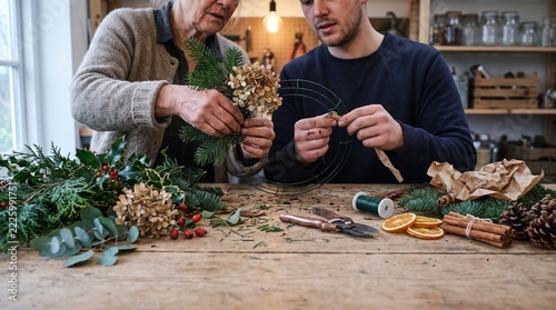 Senior Woman and Young Man Making Christmas Wreath in Rustic Workshop