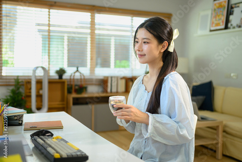 Obraz na plátně Young Woman Enjoying Coffee Break at Home Office Desk, Smiling While Holding Gla