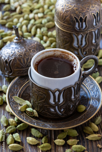 Traditional coffee served in ornate cup with cardamom pods on wooden table