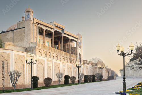 Hazrat Khizr mosque in Samarkand with ornate brick facade and carved wooden veranda along an empty boulevard. Ideal for travel guides, cultural publications, and tourism marketing materials.