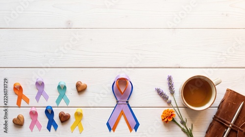 Awareness ribbons with tea and journal on white wooden background