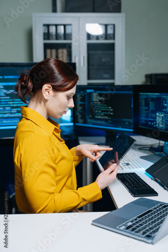Focused female programmer working on software development and cybersecurity using multiple monitors and a tablet in a modern IT office. Advanced tech and data analysis.