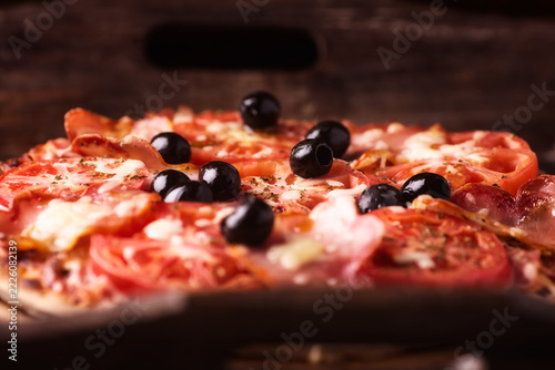 Pizza with ham, mozzarella cheese and tomatoes . Rustic wooden background. Soft focus.